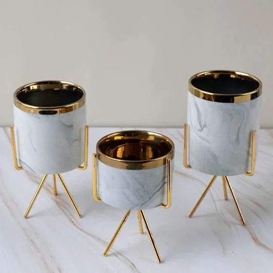 Luxury marble finish metal planter pots with gold stands arranged together for sophisticated home decor displays.