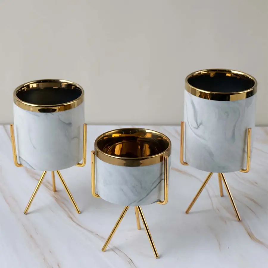 Luxury marble finish metal planter pots with gold stands arranged together for sophisticated home decor displays.