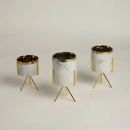 A white marble finish planter with a gold metal stand placed on a bright surface highlighting its sleek modern shape and elegant style.