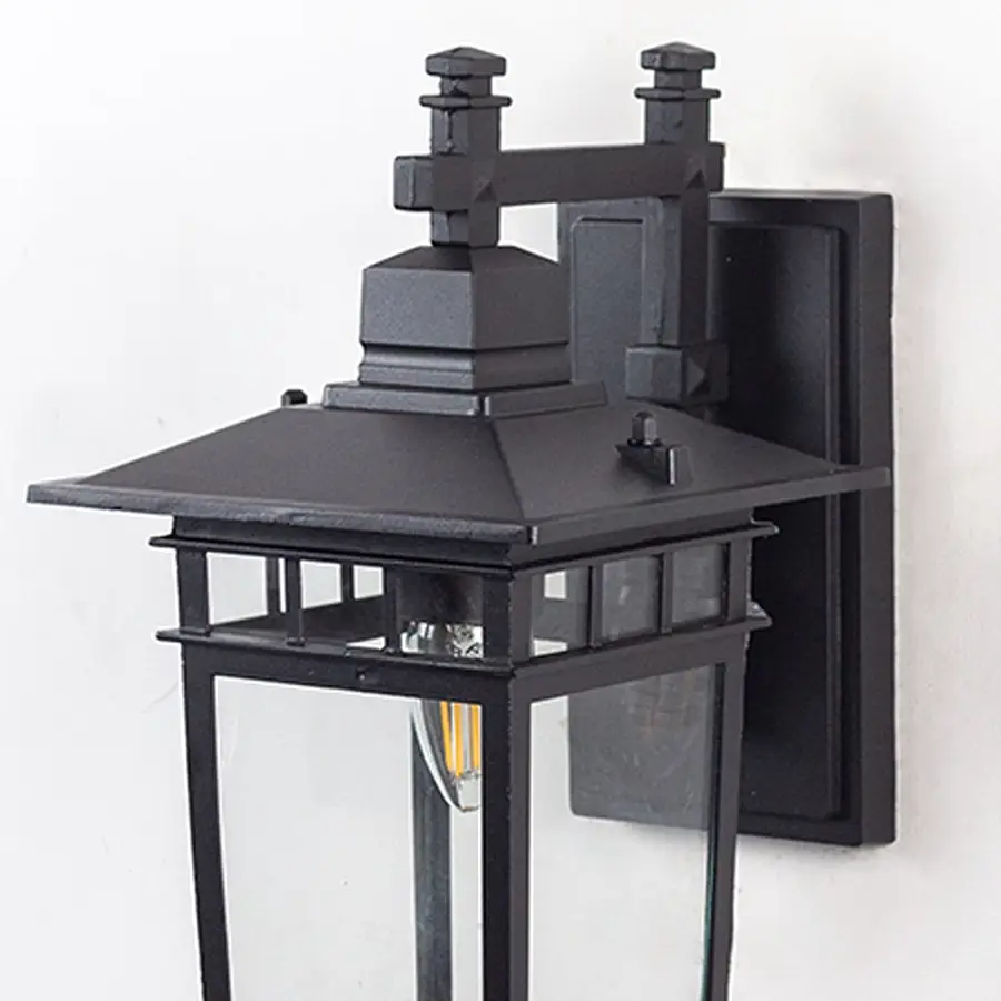 Closeup of outdoor wall lantern light with black frame clear glass and glowing bulb for modern home exteriors.