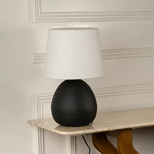 Black ceramic table lamp with rounded matte base and white fabric shade for modern interior decor styling.