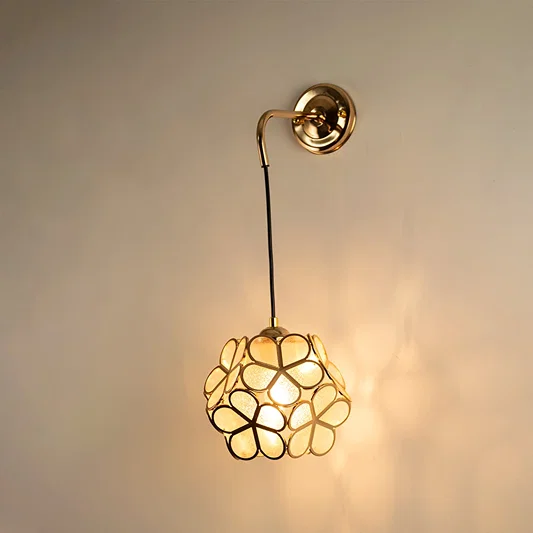 Artistic gold wall light with floral metal frame glowing softly on white background creating warm ambience.