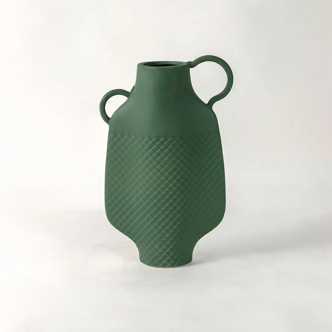 Green ceramic vase with dual side handles and textured surface placed on white surface against neutral background enhancing contemporary home decor aesthetic.