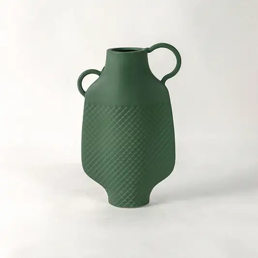 Green ceramic vase with dual side handles and textured surface placed on white surface against neutral background enhancing contemporary home decor aesthetic.