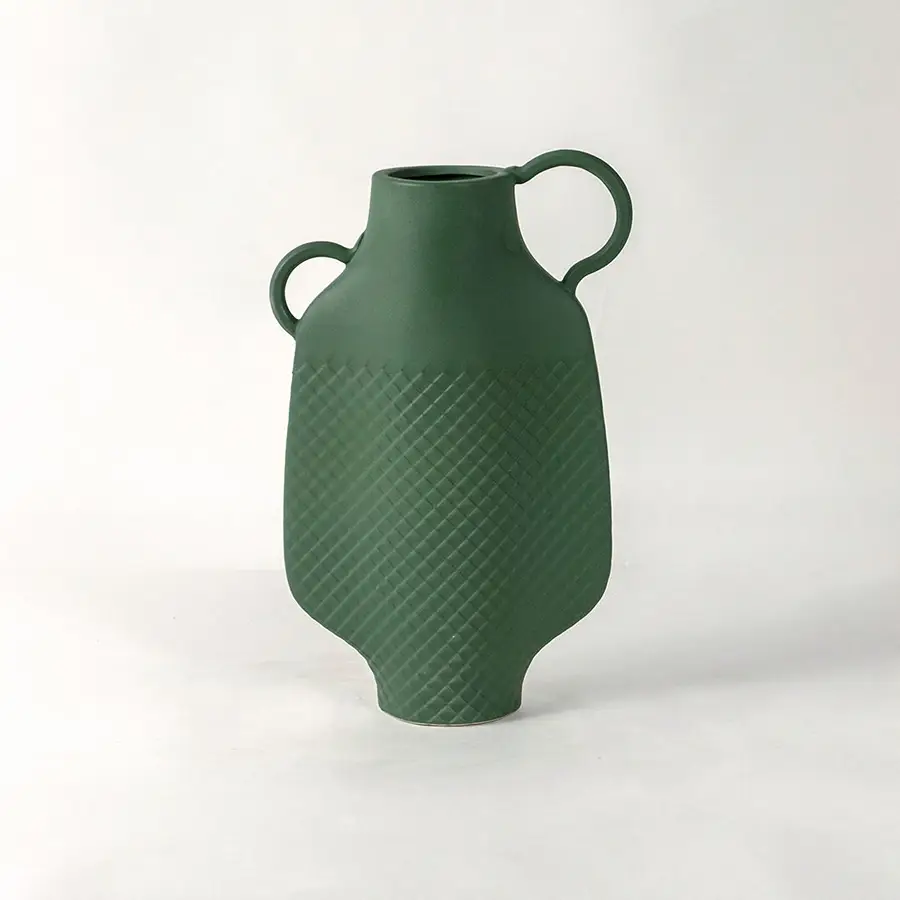 Green ceramic vase with dual side handles and textured surface placed on white surface against neutral background enhancing contemporary home decor aesthetic.