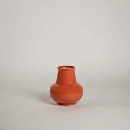 Matte terracotta orange ceramic bud vase with a round bulbous base and flared neck on white background for minimal art.