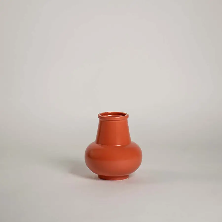 Matte terracotta orange ceramic bud vase with a round bulbous base and flared neck on white background for minimal art.