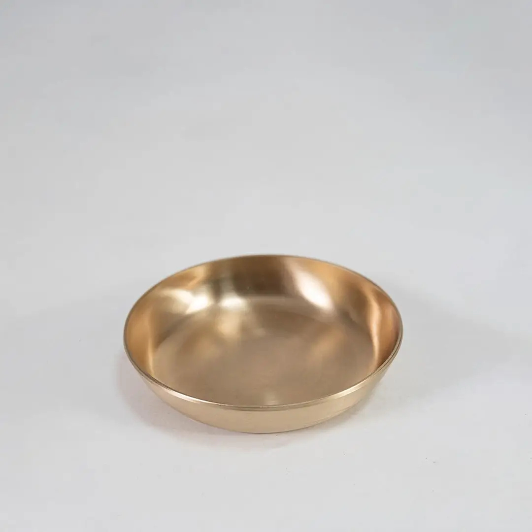 Single round brass bowl with smooth interior and matte gold finish placed centrally on white background surface.
