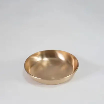 Single round brass bowl with smooth interior and matte gold finish placed centrally on white background surface.