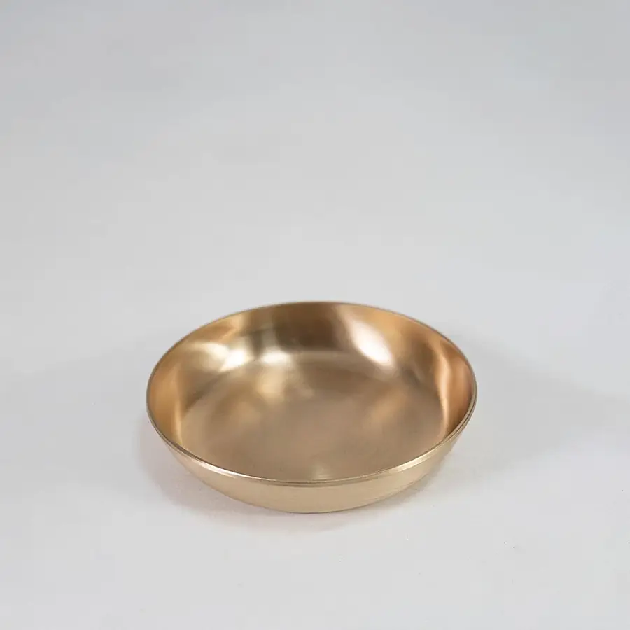 Single round brass bowl with smooth interior and matte gold finish placed centrally on white background surface.