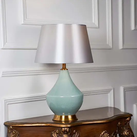 White fabric shade table lamp with glossy mint ceramic base and gold accent casting warm ambient light on side table.