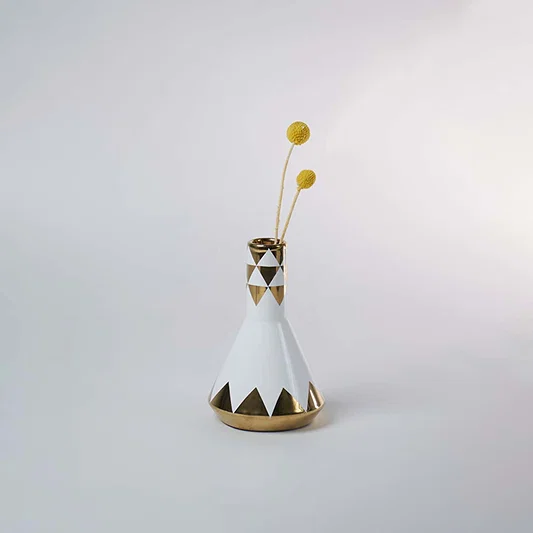 Stylish white and gold ceramic vase with geometric patterns placed with minimal decor in a bright modern setting.