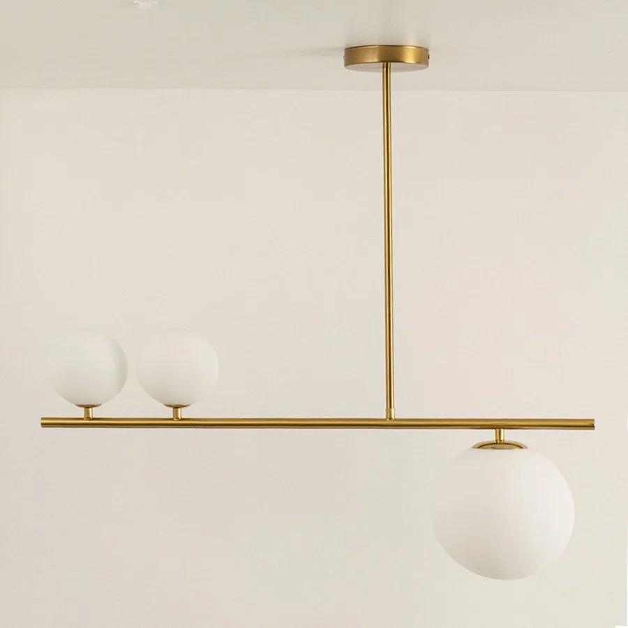 Gold linear chandelier displayed with lights off showing sleek frame frosted glass globes and modern minimalistic aesthetic design.