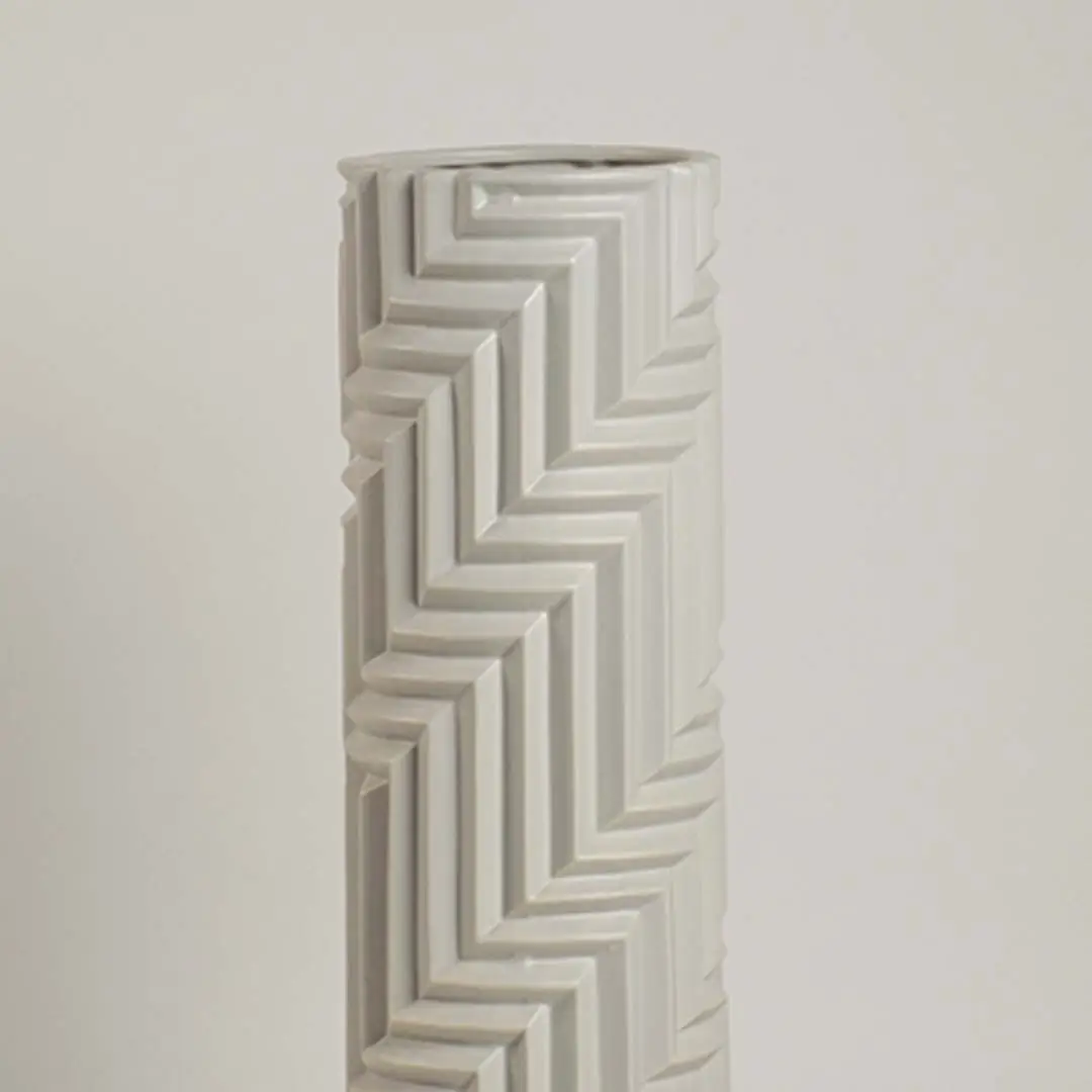 Minimal white ceramic vase with raised zigzag patterns captured in soft ambient light emphasizing its sculptural details.