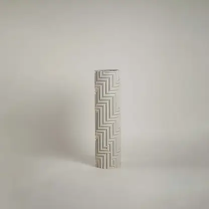 White geometric ceramic vase with angular embossed design highlighted under warm light against a white background for contrast.