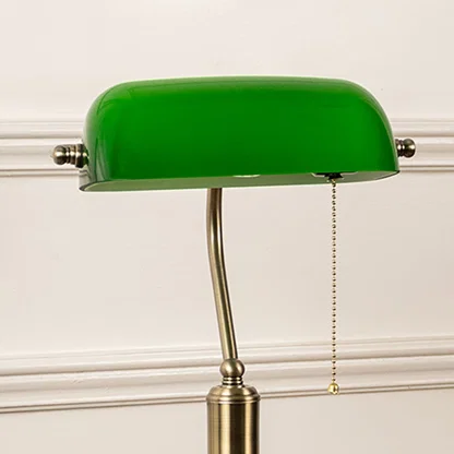 Closeup of green glass banker lamp highlighting antique brass base and pull chain switch for timeless decor charm.