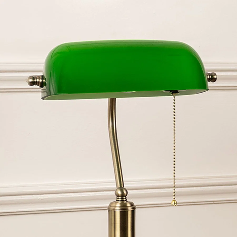 Closeup of green glass banker lamp highlighting antique brass base and pull chain switch for timeless decor charm.
