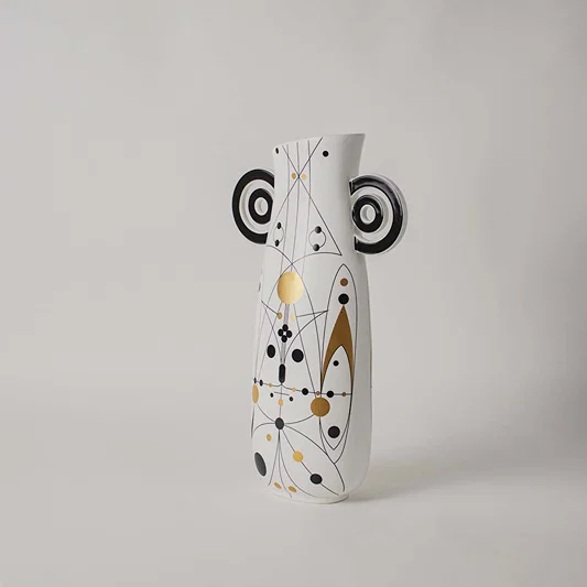 White ceramic vase featuring geometric gold and black line patterns and circular loop handles on clear white background.