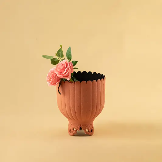 Matte terracotta ribbed metal planter with pink flowers for warm modern home decor and artistic accents.