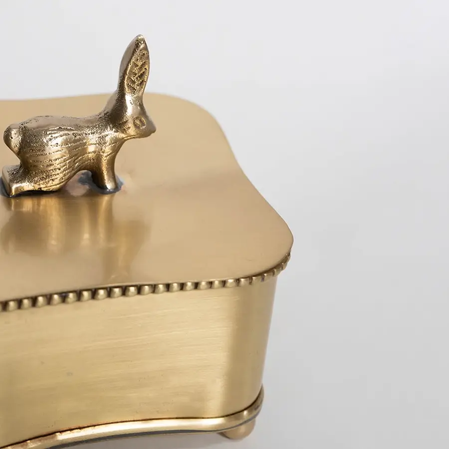 Main image of gold-toned storage box with bird-shaped handle lid and footed base shown on white background.