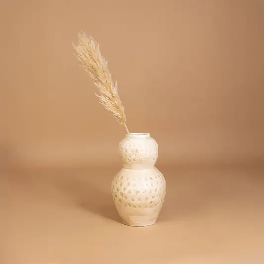 Cream textured decorative vase with polka dot design placed in a styled interior adding warm artistic decor to shelves consoles and living spaces.