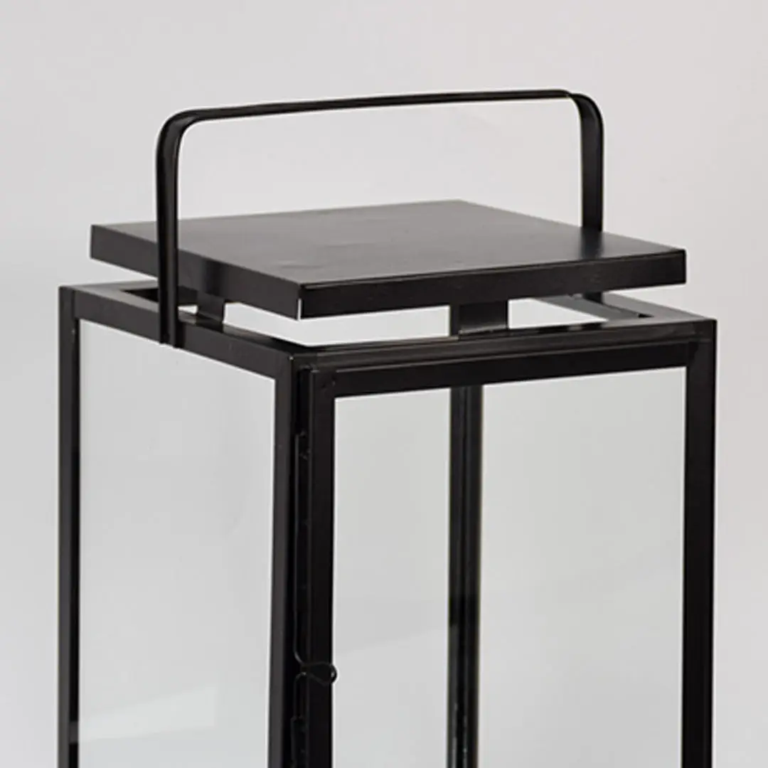 Closeup of black metal lantern with flat top handle for modern indoor decor styling use.
