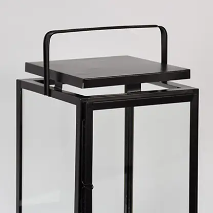 Closeup of black metal lantern with flat top handle for modern indoor decor styling use.