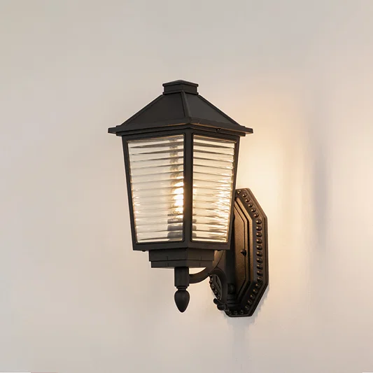 Black metal outdoor wall light on white background with ribbed glass shade for modern patio decor.