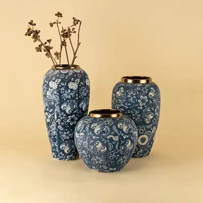 Decorative blue ceramic vases with floral pattern and dried stems placed on beige surface against warm background showcasing coordinated modern home decor arrangement.
