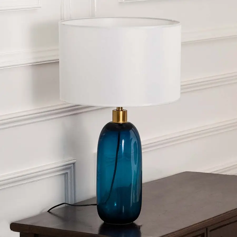 White shade blue glass lamp on wooden table with light on and white wall background for clean modern décor.