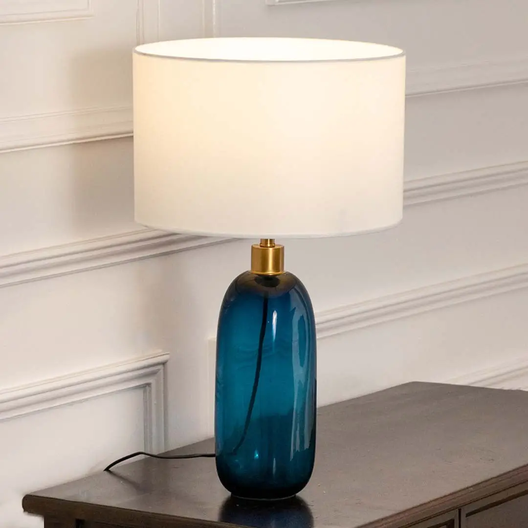 Blue glass table lamp with fabric shade placed on a wooden console table creating refined contemporary lighting.