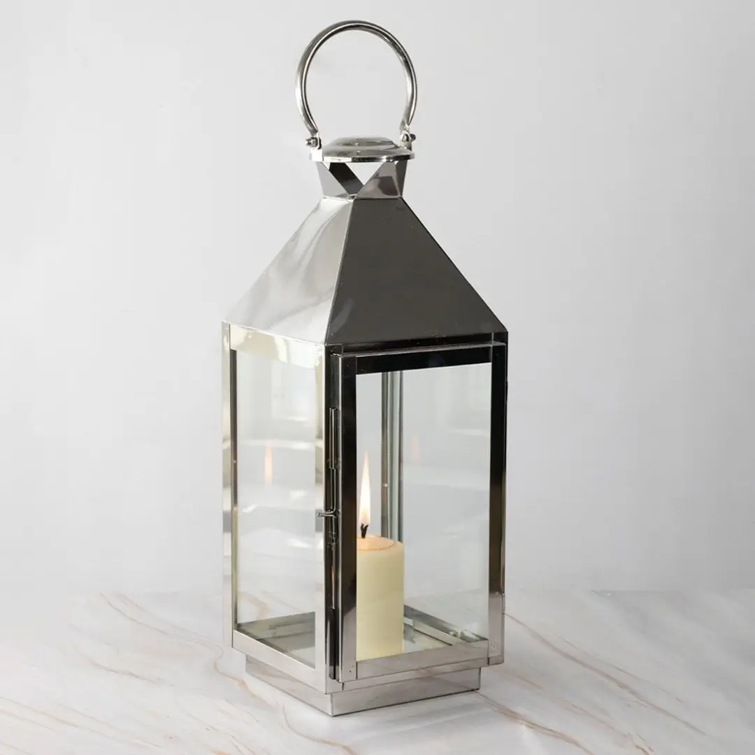 Large silver lantern with candle lit glowing softly against black background for stylish home lighting.
