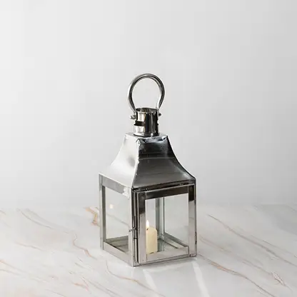 Silver lantern lit shown plain on white background highlighting polished stainless steel frame.