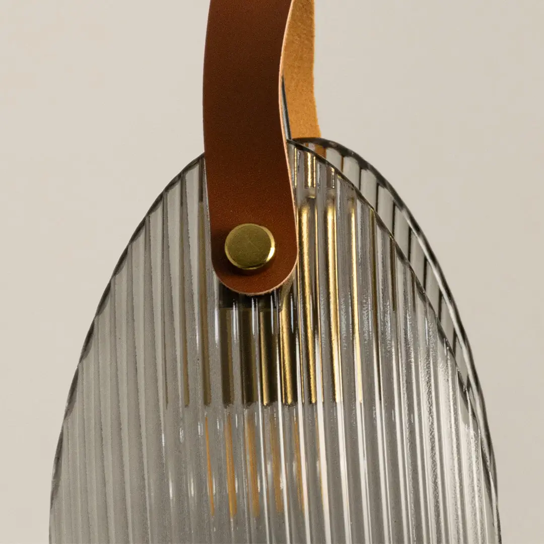 Closeup of gold metal wall light with ribbed glass shade and leather strap detail on white background ideal for modern interior decor.