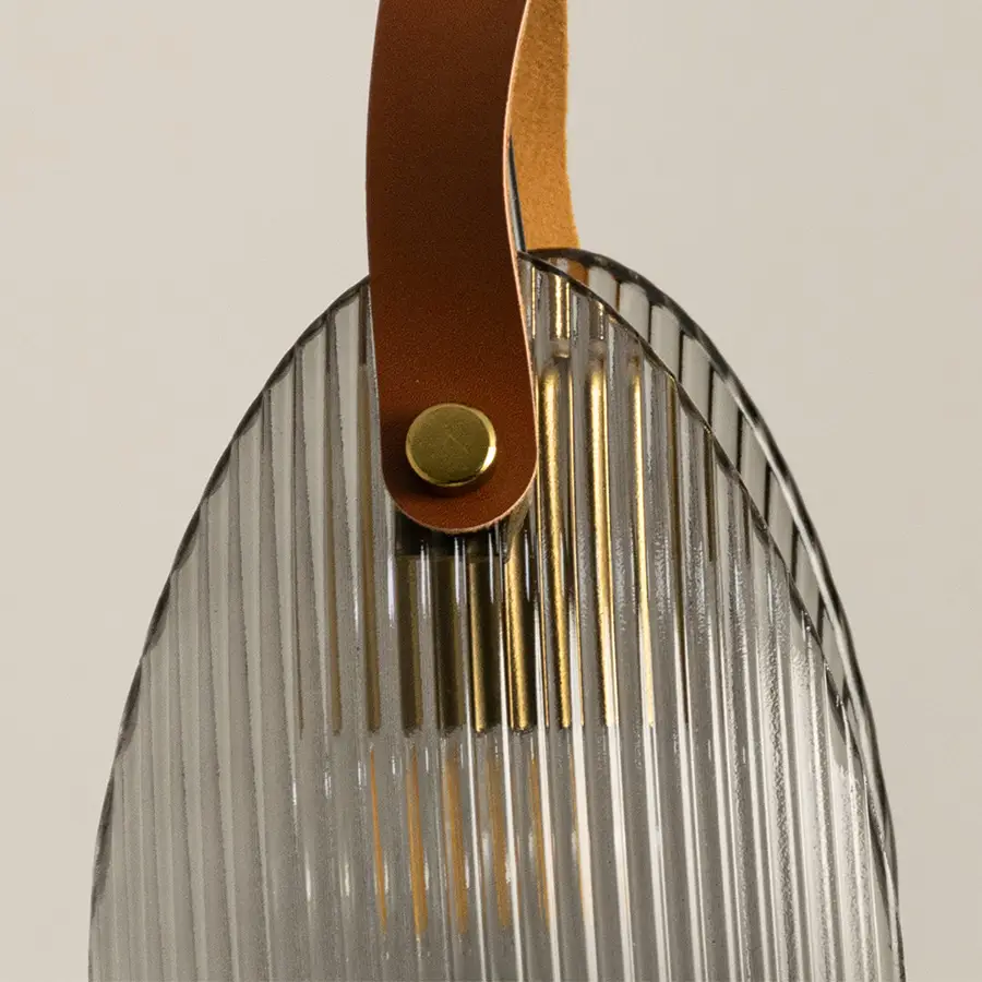 Closeup of gold metal wall light with ribbed glass shade and leather strap detail on white background ideal for modern interior decor.
