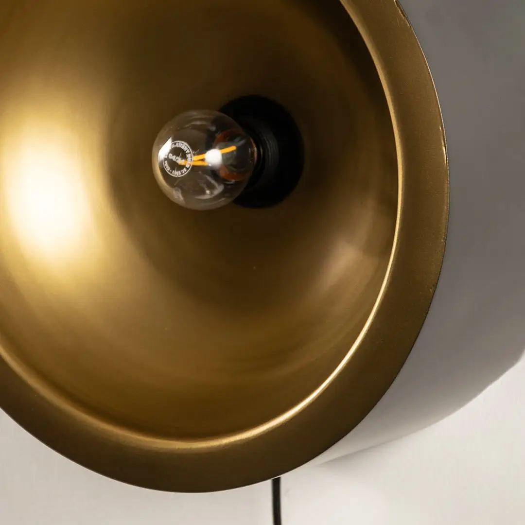 Detailed macro view looking inside a brushed gold metal cup wall lamp shade highlighting the round glass light bulb.