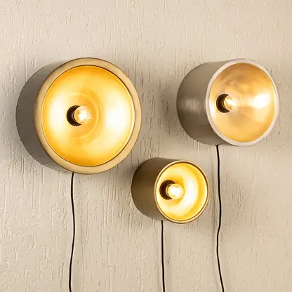 Trio of modern gold and silver cylinder cup wall sconce lamps casting a warm glow clustered on a textured beige wall.