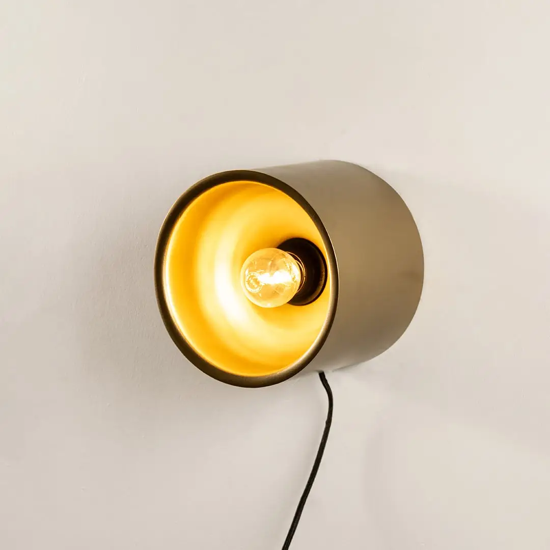 Contemporary matte gold metal cylinder wall light fixture turned on showing a bright golden interior illumination.