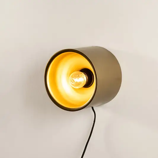 Contemporary matte gold metal cylinder wall light fixture turned on showing a bright golden interior illumination.