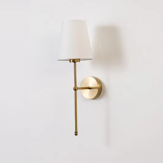 Gold wall light with a white shade displayed on a white background showing its elegant minimal shape.