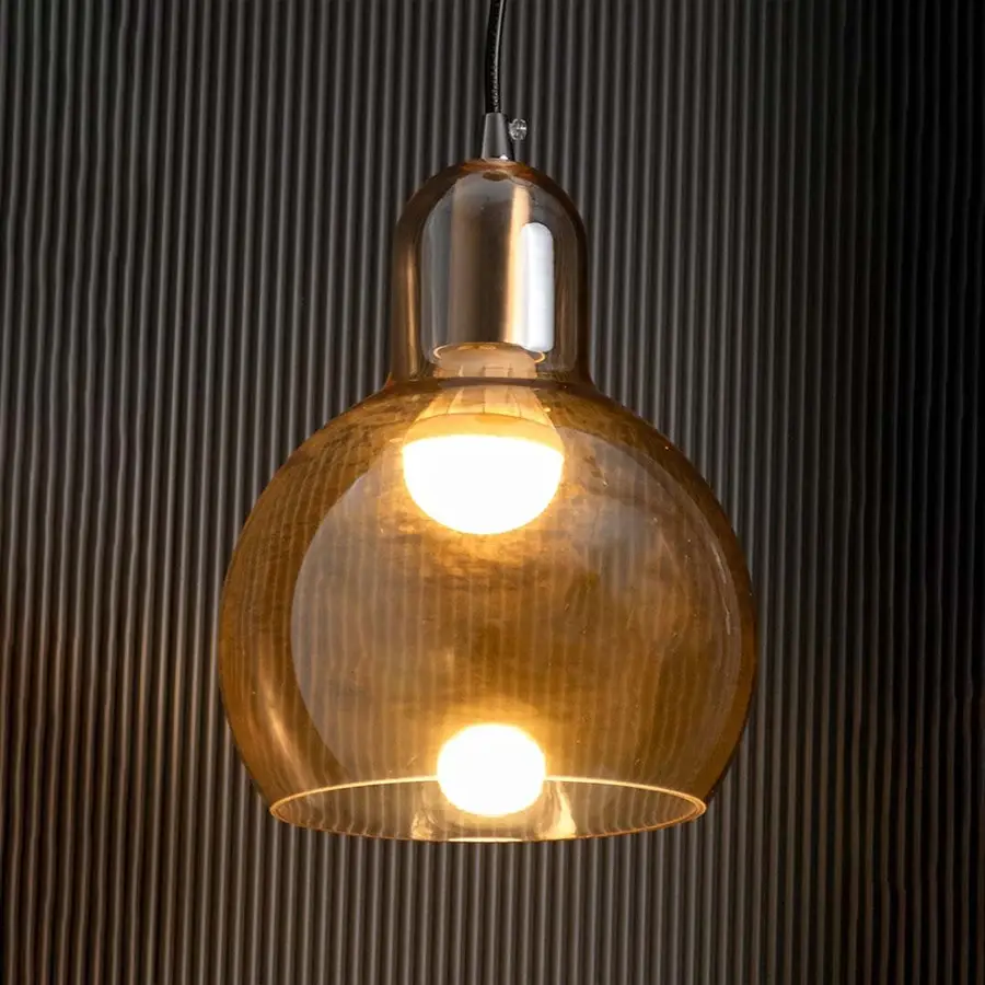Amber glass pendant light glowing warmly with visible bulb gold metal holder creating ambient lighting on dark wall.