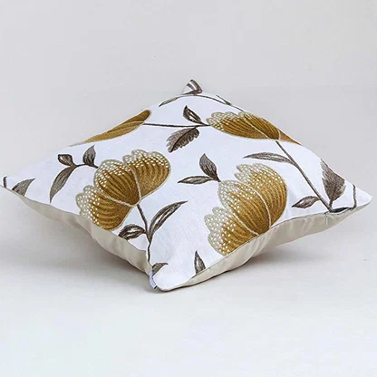 White cotton cushion cover with large golden botanical motifs shown at an angle adding a premium nature inspired décor accent with a soft breathable and skin friendly fabric.