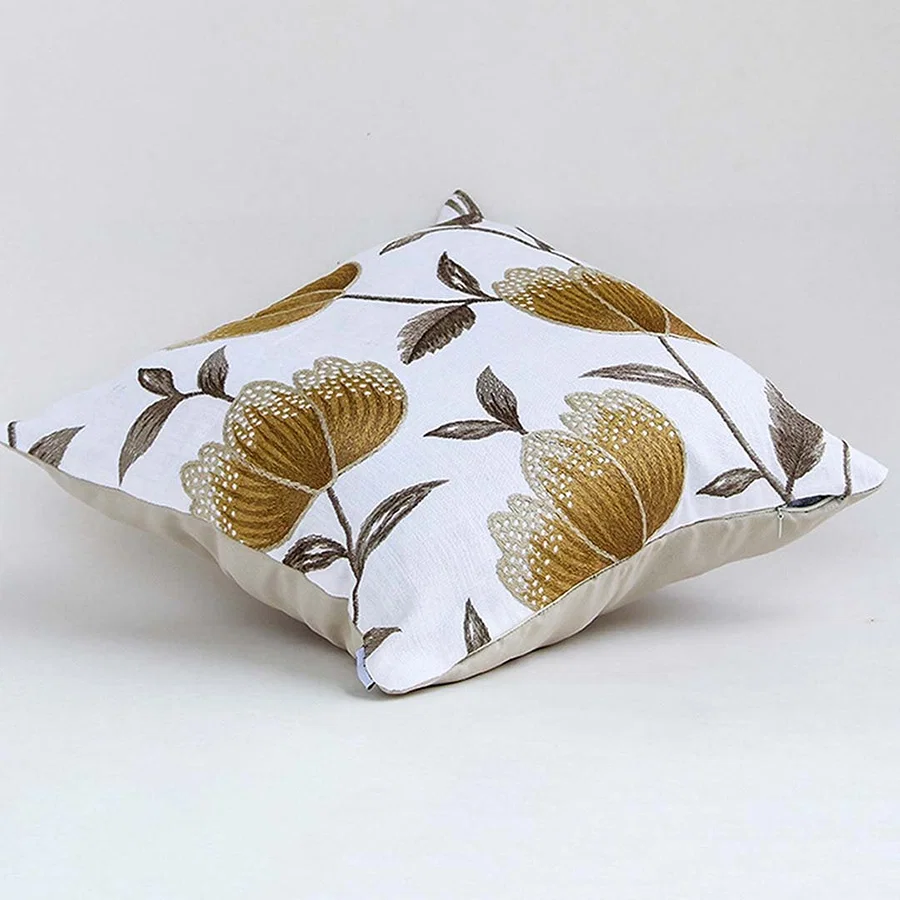 White cotton cushion cover with large golden botanical motifs shown at an angle adding a premium nature inspired décor accent with a soft breathable and skin friendly fabric.