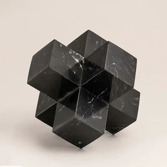 Black marble geometric sculpture with sharp angles displayed on a white background highlighting its design.