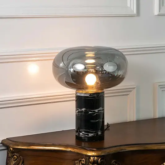 Smoked glass table lamp with black marble base and exposed bulb designed for sophisticated modern table lighting.