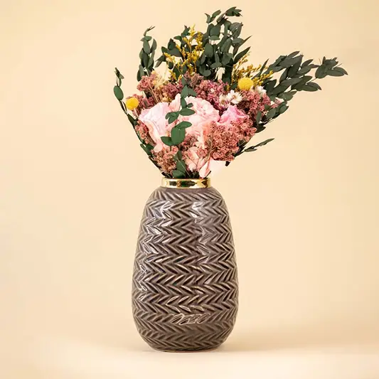 Grey zigzag ceramic vase with gold rim decorated with pink and yellow dried flowers against a beige background for elegant home decor.