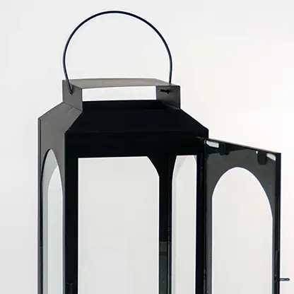 Closeup of black metal lantern with open glass door and hanging loop for tabletop decor styling.