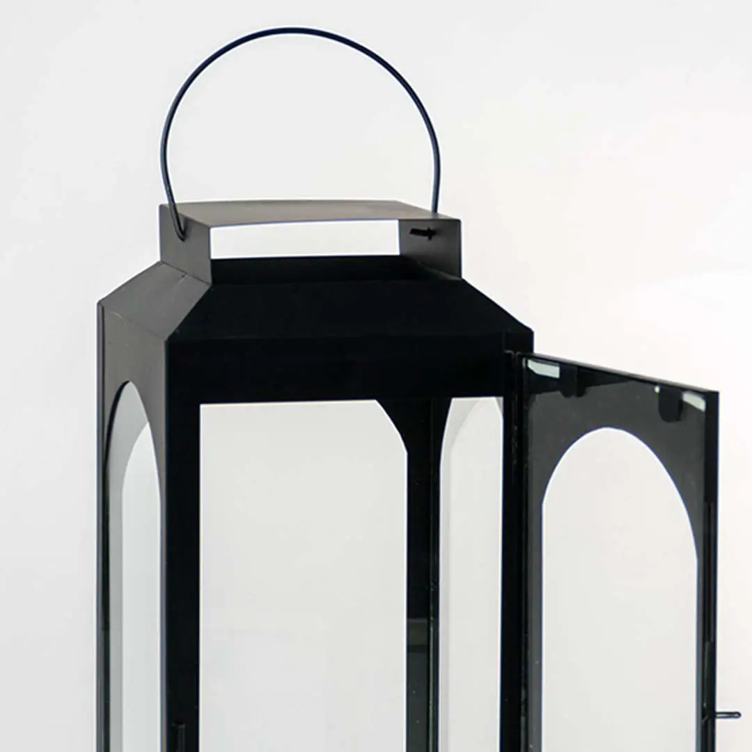 Closeup of black metal lantern with hanging handle and glass panels for modern decor styling use.