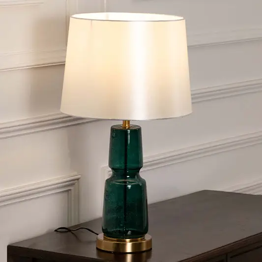 Emerald green ceramic table lamp with fabric shade placed on a wooden console table creating elegant ambient lighting.