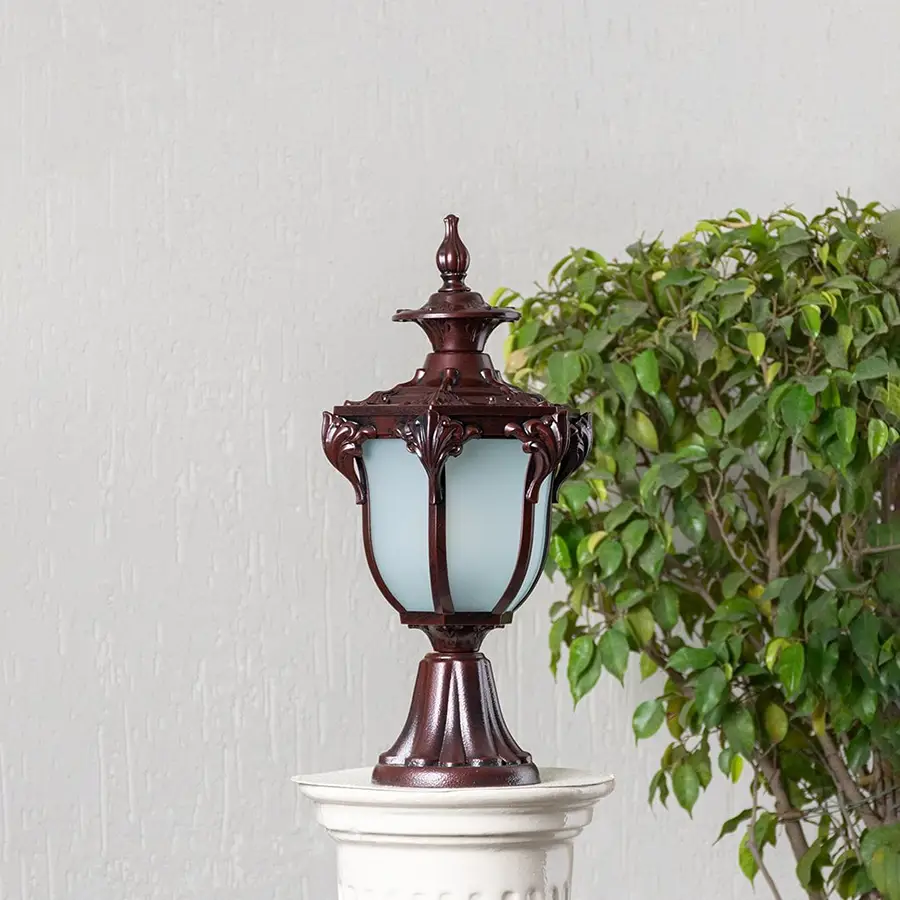 Classic outdoor brown pillar lamp with frosted glass shade and ornate design placed on stone base for garden and patio.